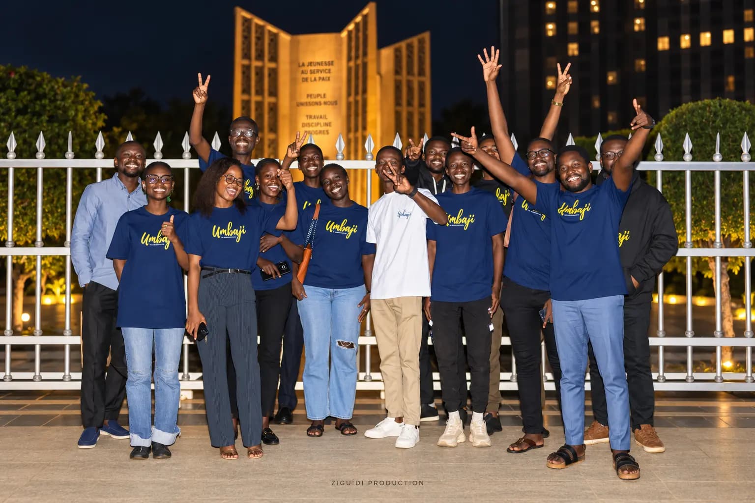 The Umbaji team gathered at night in front of a lit monument, wearing Umbaji t-shirts, several with arms raised