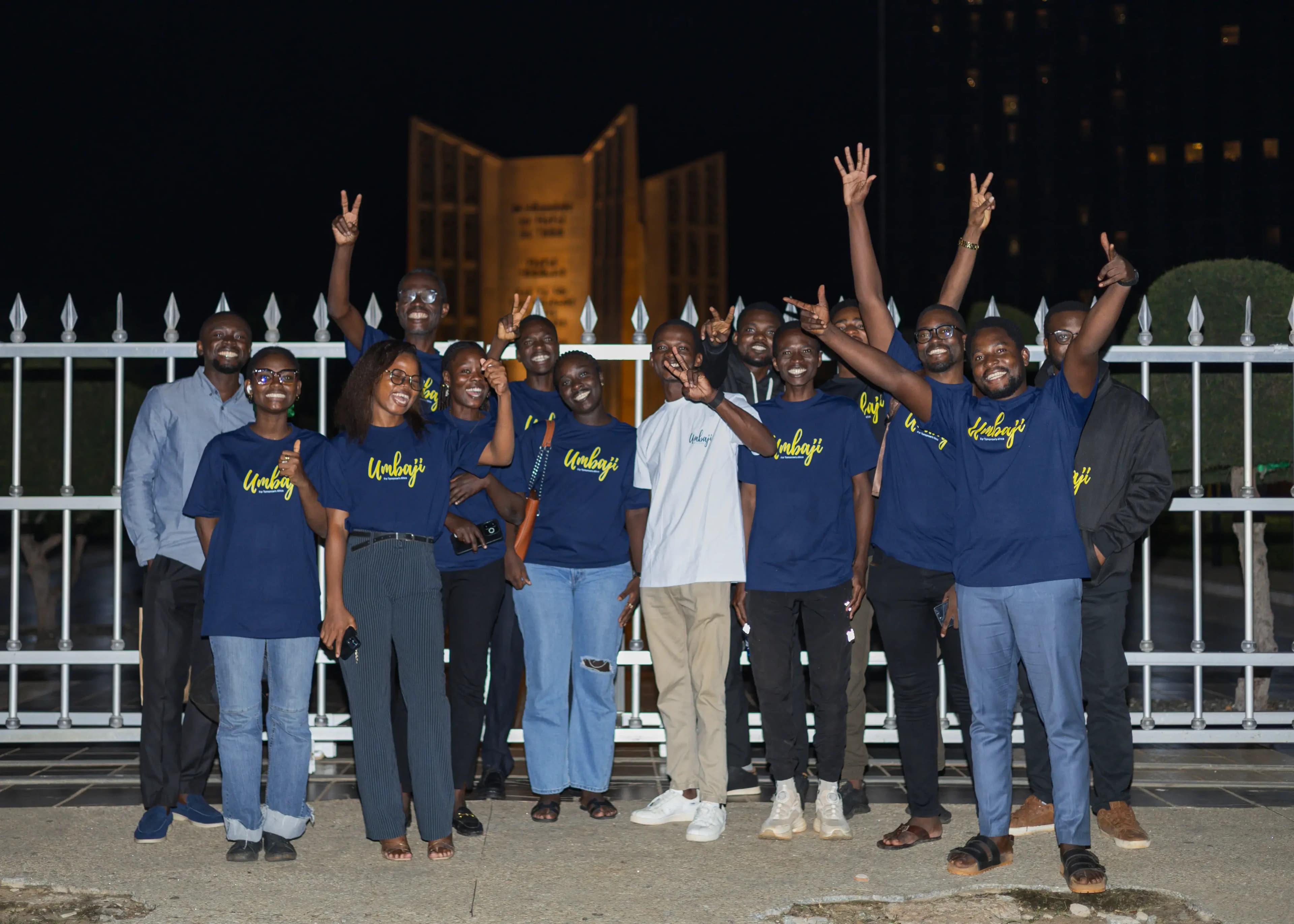 L'équipe Umbaji réunie de nuit devant un monument éclairé, en t-shirts Umbaji, plusieurs bras levés